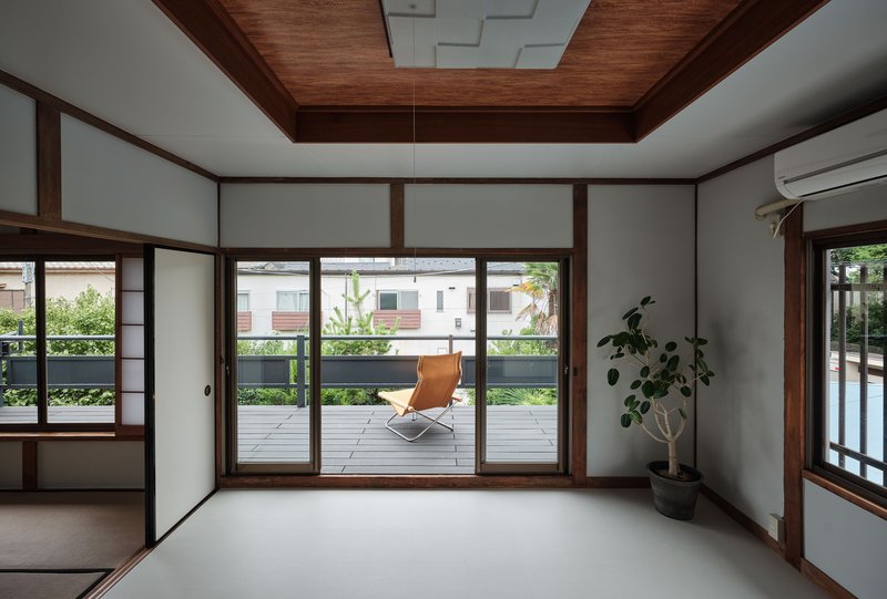 Interior room with timber-framed sliding doors opening onto a terrace with a single chair and potted plant