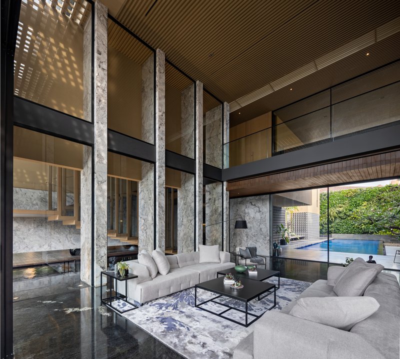 Double-height living room with concrete columns, steel mezzanine bridge and timber slat ceiling filtering daylight