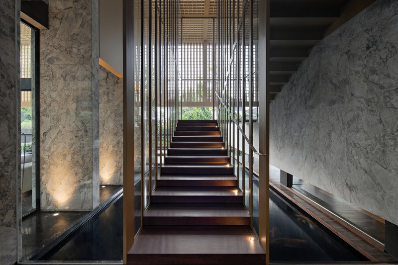Timber staircase with integrated lighting rising between vertical steel louvers and textured stone walls