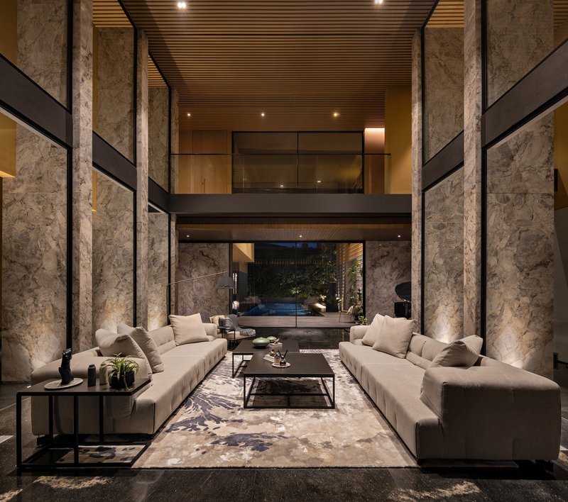 Double-height living space with rough stone columns and slatted timber ceiling under evening light