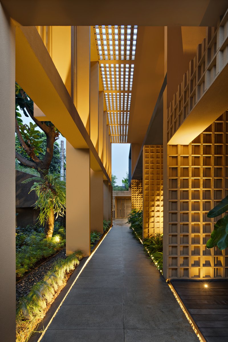 Narrow entry corridor with perforated brick screens overhead and uplighting along planted edges at dusk