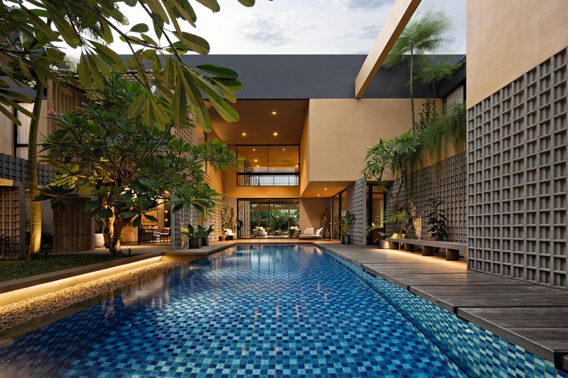 Courtyard pool extending toward the double-height glazed living space framed by tropical plantings