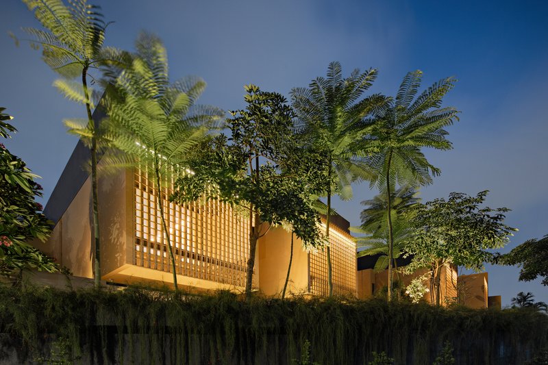 Elevated view of the lattice brick volumes rising above hedge and palm trees at dusk