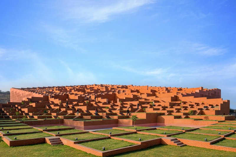 Stepped facade of orange brick volumes cascading down to a grid of lawn courtyards under clear sky