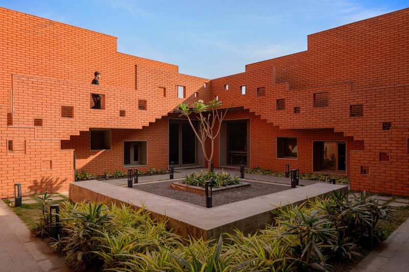 Raised concrete planter bed surrounded by brick walls with scattered window openings at dusk