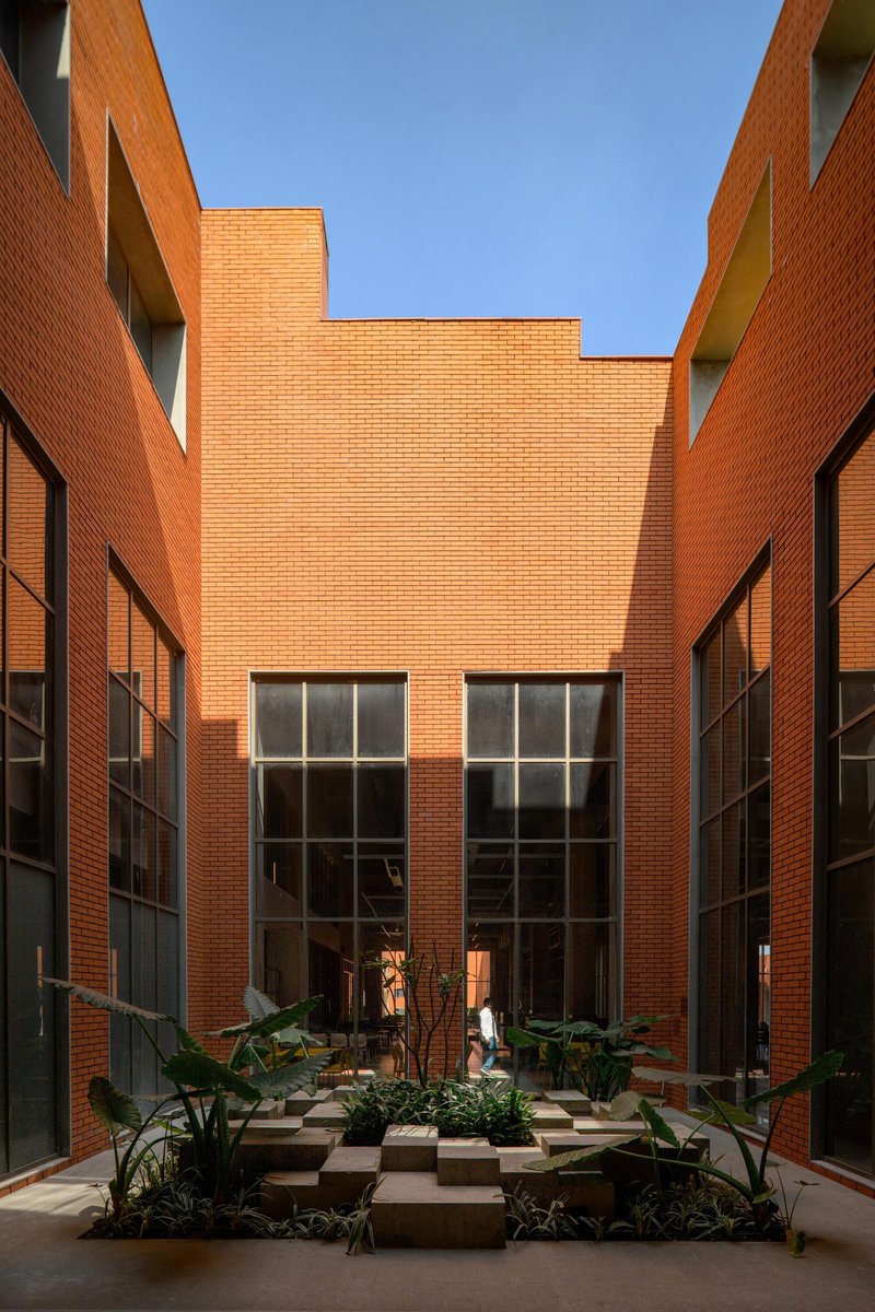 Narrow courtyard passage with tall brick walls and large gridded windows under bright midday sun