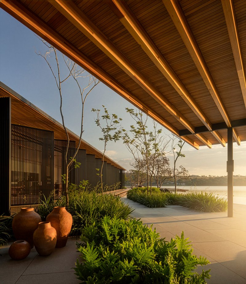 Covered terrace with exposed timber beams and planted beds overlooking the lake at sunset