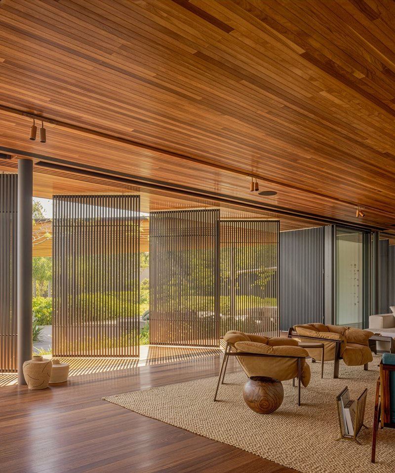 Living room with vertical timber screens filtering afternoon light across wood flooring and furniture