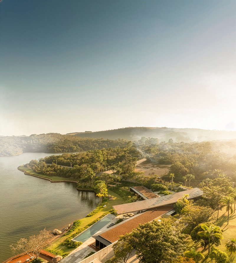 Aerial view of the low-slung residence with sweeping roofline along a forested peninsula at golden hour