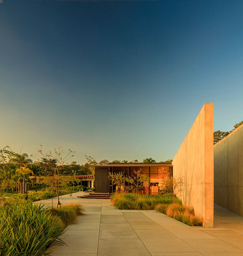 Concrete walkway flanked by planted beds leading toward timber pavilion at sunset