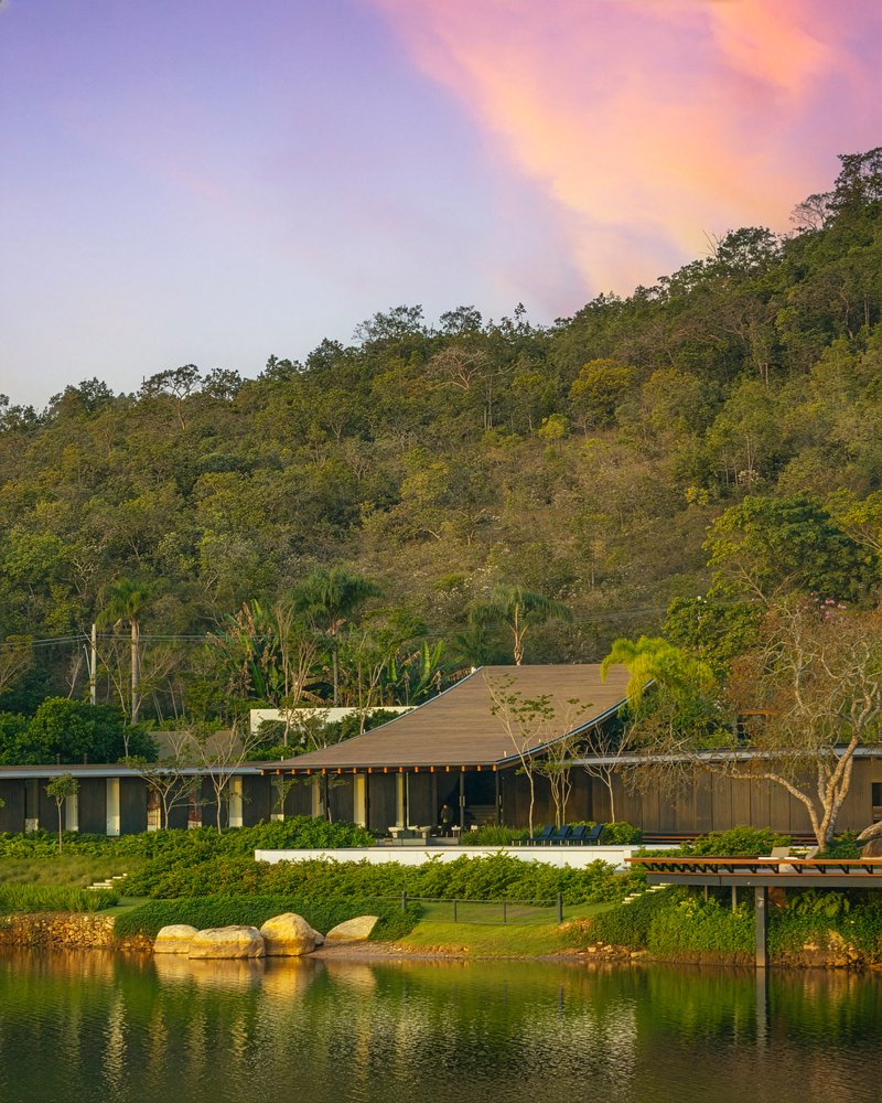 Lakeside view of the timber-roofed pavilion beneath a forested hillside at dusk