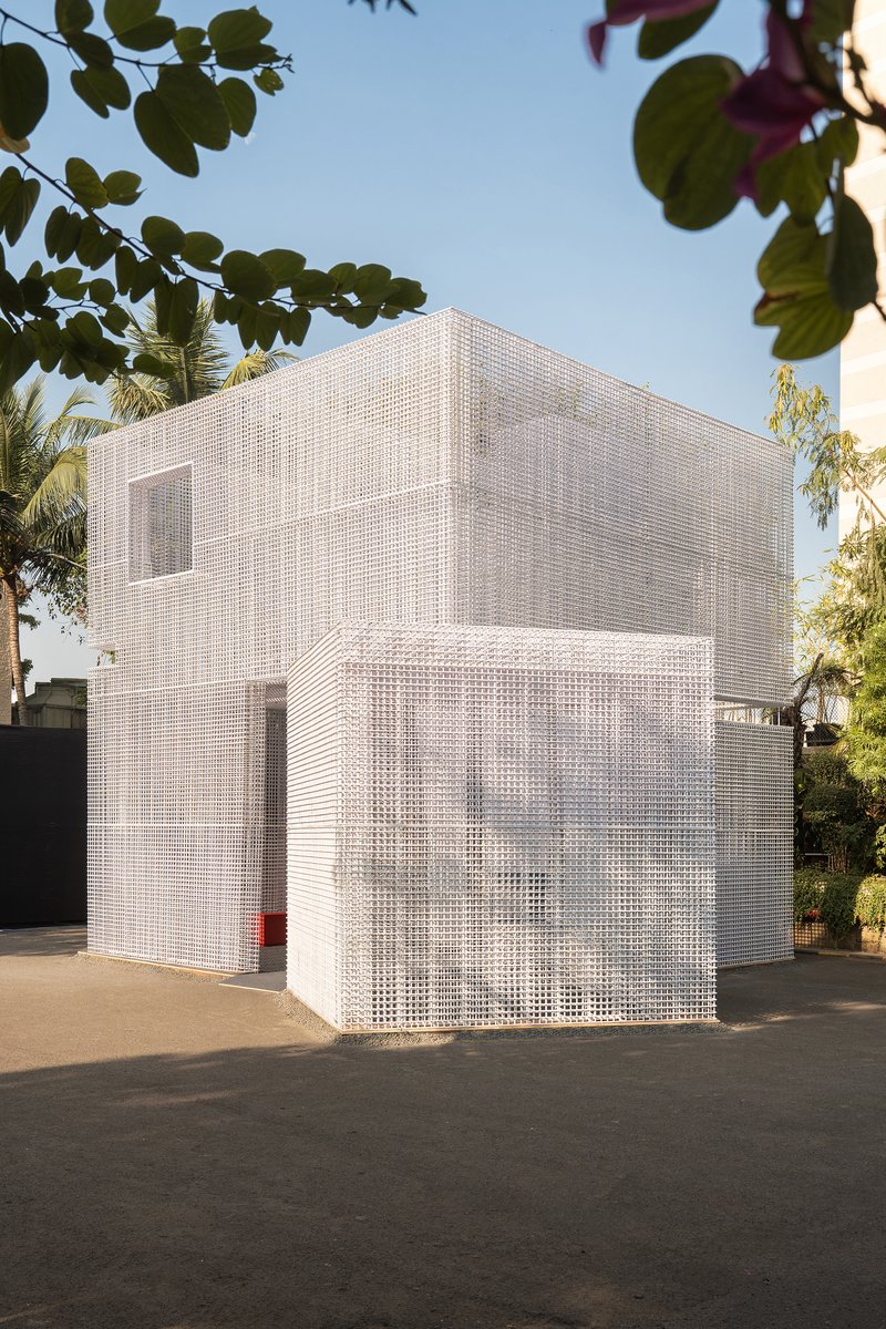 Two-story white gridded mesh facade beneath overhanging palms and leafy trees in afternoon light