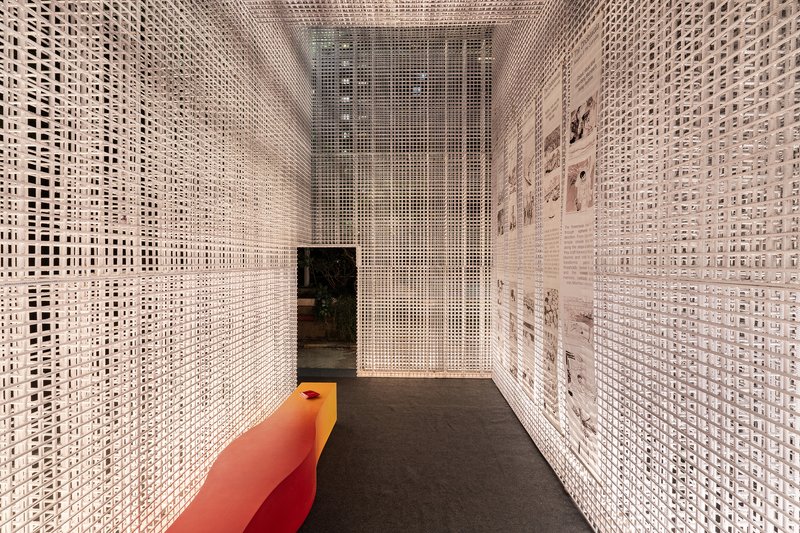 Narrow corridor enclosed by white perforated mesh screens with an orange bench and dark carpet flooring
