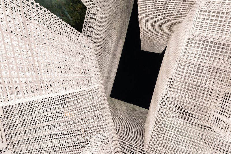 Looking up through white mesh-wrapped volumes intersecting around a dark central void