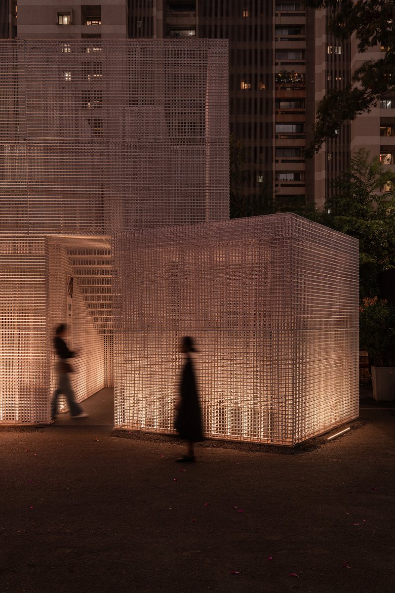 Close view of the perforated screen wall with interior staircase visible as figures pass at twilight