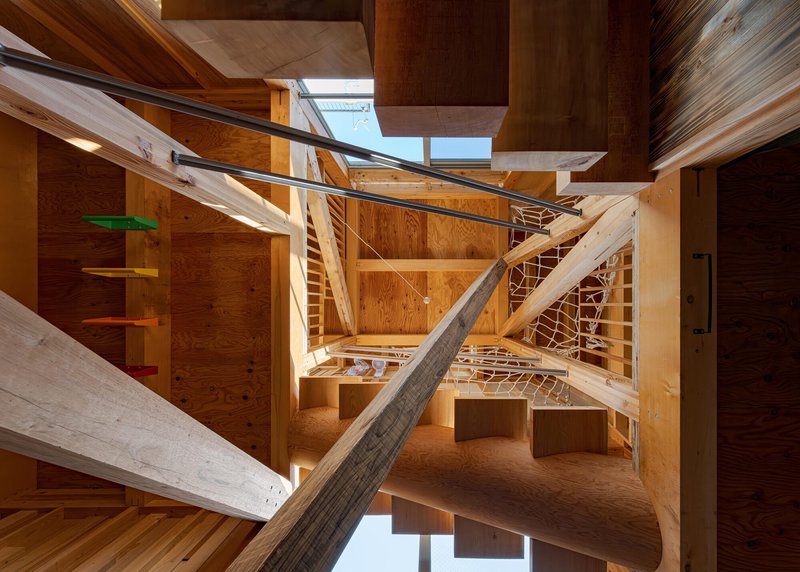 Looking up through the open timber stair structure with crisscrossing beams and skylights overhead
