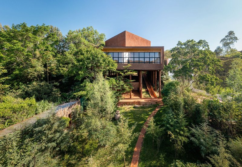 Elevated red earth structure on timber supports surrounded by terraced garden beds and native trees