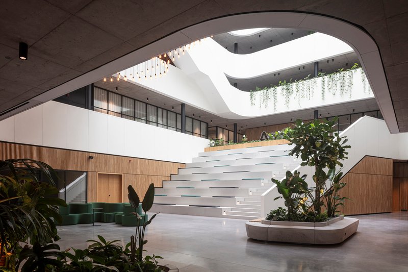 Multi-level atrium with curving white staircase, timber cladding and planters with tropical foliage below a skylight
