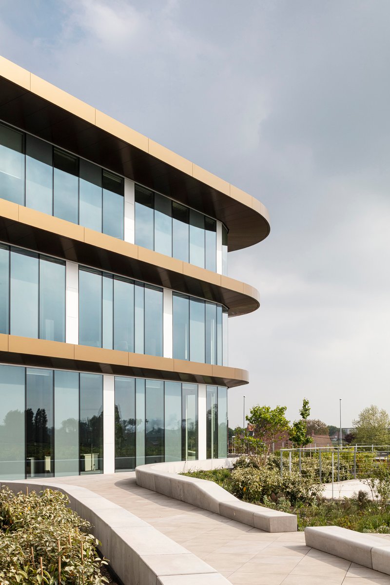 Exterior terrace with curved glass facade, stone pavers and planted beds under an overcast sky