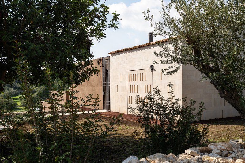 Rear elevation showing plastered wall with vertical slot windows among olive trees