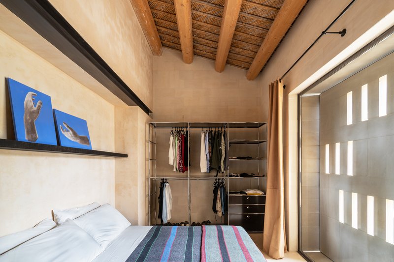 Bedroom with exposed timber ceiling beams and open wardrobe screened by curtain beside tall window slits