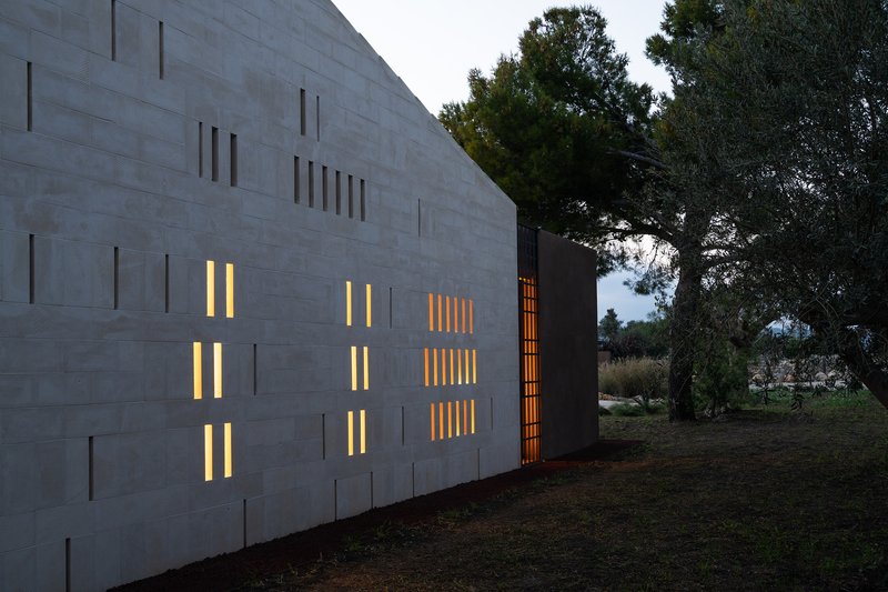 Close-up of the concrete block facade with rhythmic vertical window slits lit from within at dusk