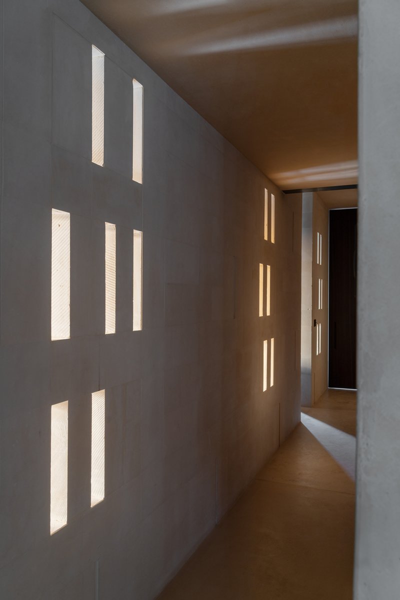 Narrow corridor with vertical slot windows casting warm light on earthen walls