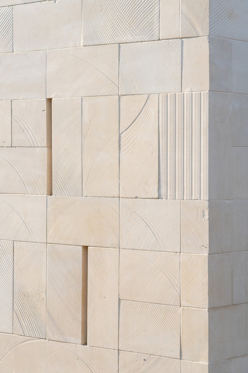 Close-up of pale limestone wall cladding with varied surface textures including smooth, striated, and fluted finishes
