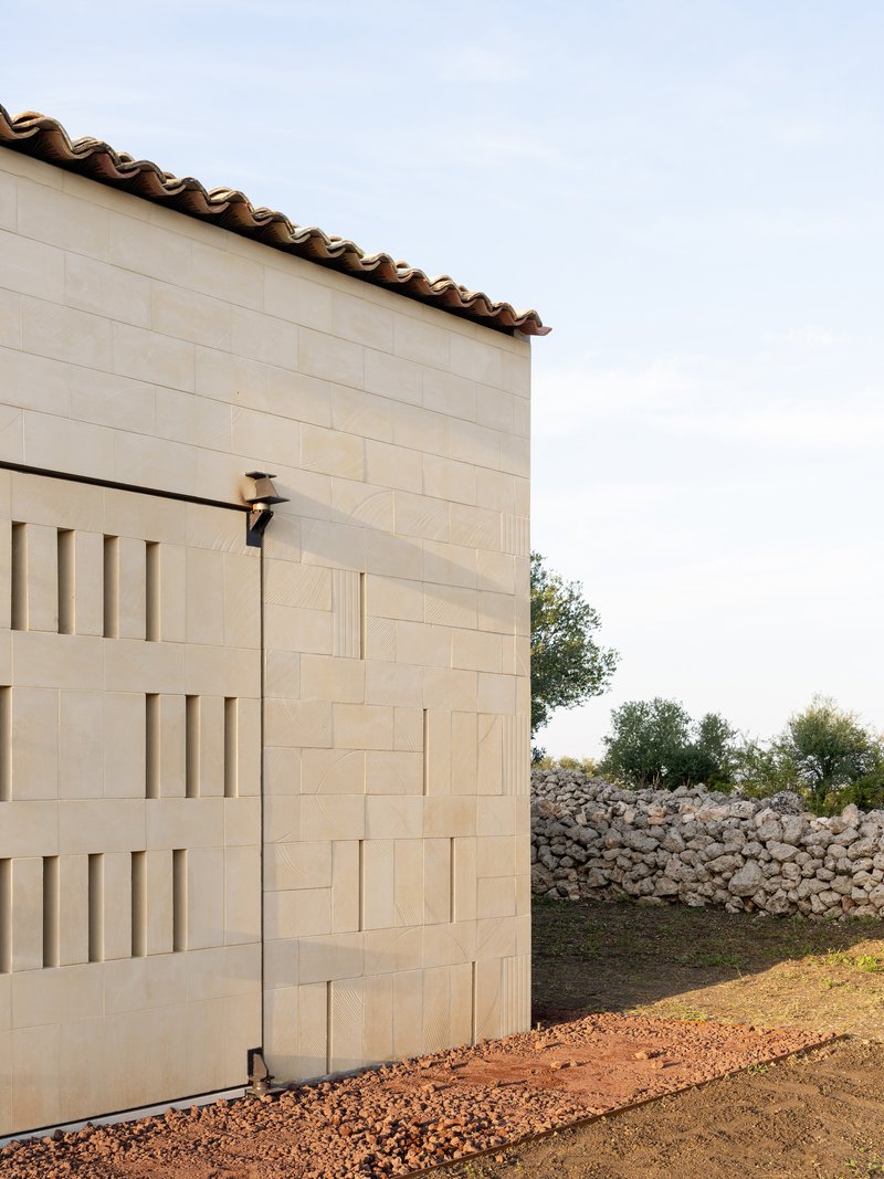 Limestone block facade with terra cotta barrel tile roof edge and dry stone wall beyond under open sky