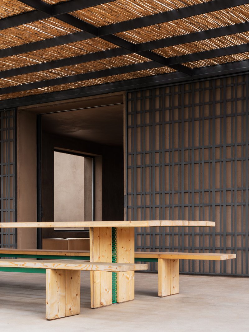Covered porch with timber bench and woven reed ceiling over gridded brick screen wall in afternoon light