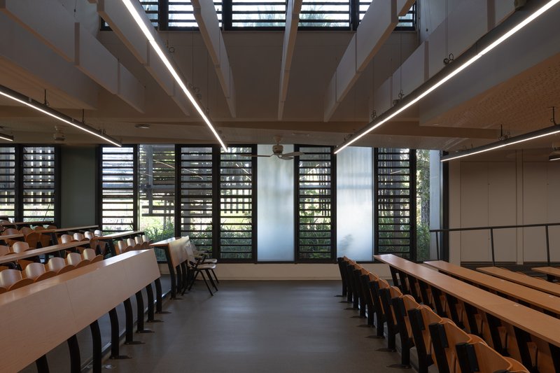 Interior hall with tiered timber benches and horizontal louvered windows beneath exposed roof structure with linear lighting