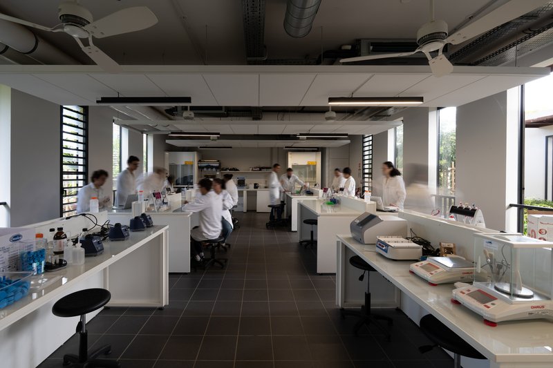 Laboratory interior with white bench islands, exposed ceiling ducts and researchers in white coats at work