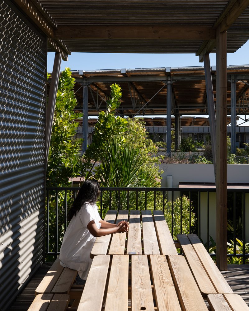 Timber deck with bench seating and metal screen wall overlooking planted terraces and timber pergola structure