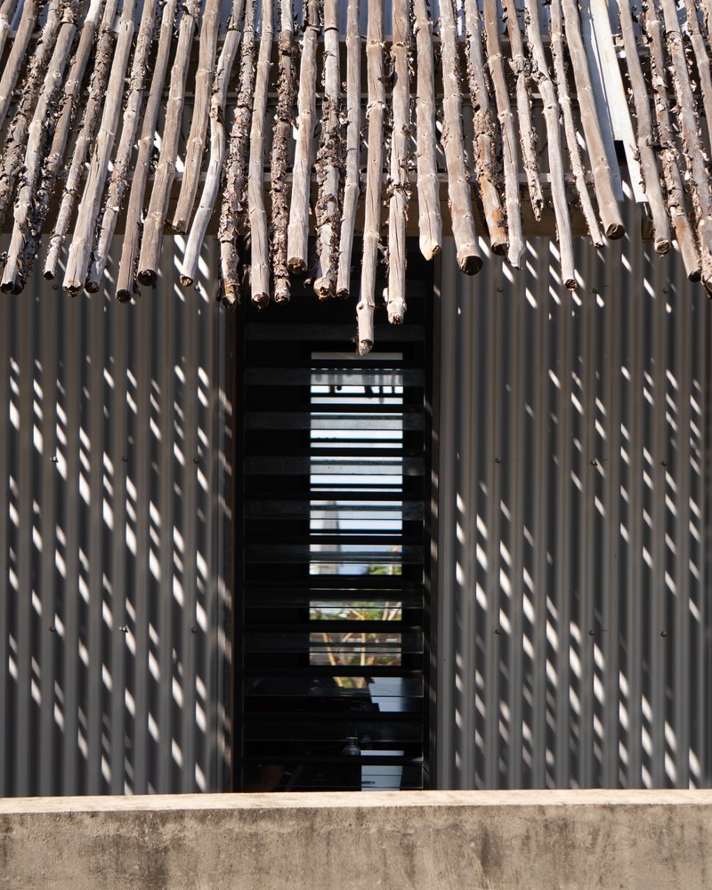 Facade of vertical timber slat screen with metal louvered window opening casting shadows in sunlight