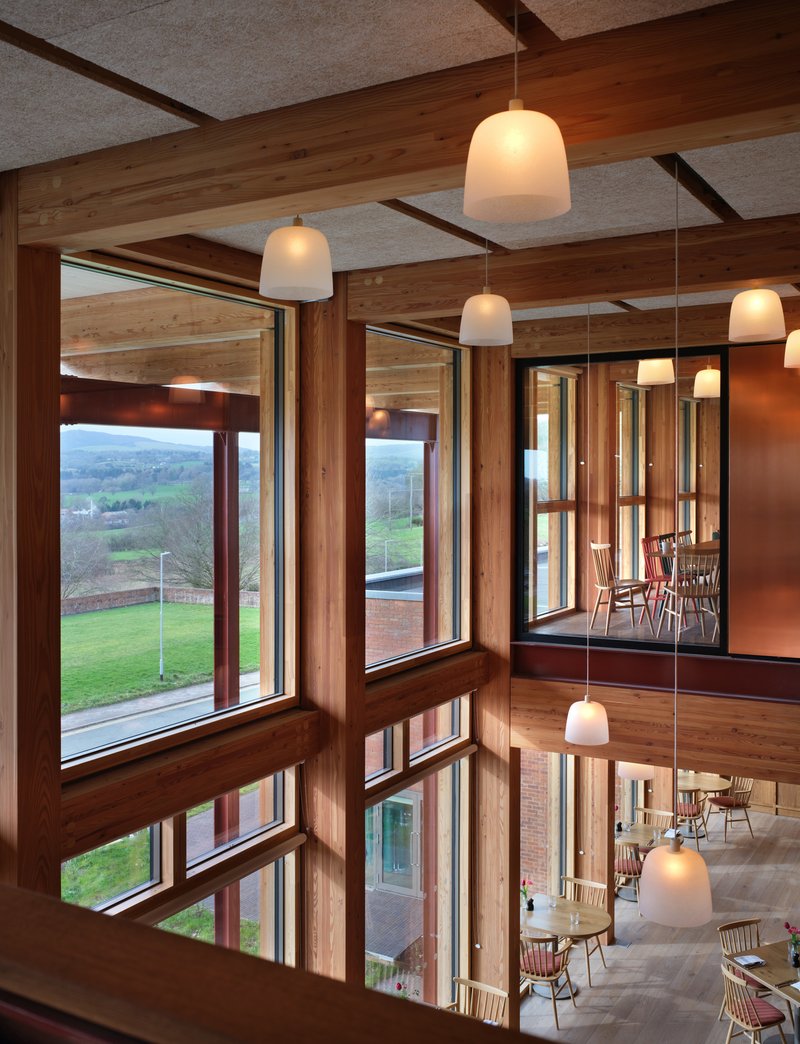 Corner windows framing countryside view with timber mullions and pendant lights reflected in glass
