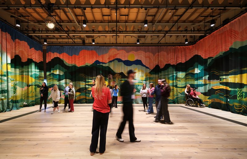 Interior hall with colorful landscape mural on glass partition and people gathered in groups