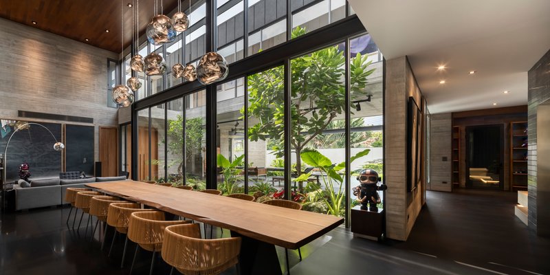 Dining space with long timber table beneath clustered pendant lights adjacent to a planted atrium