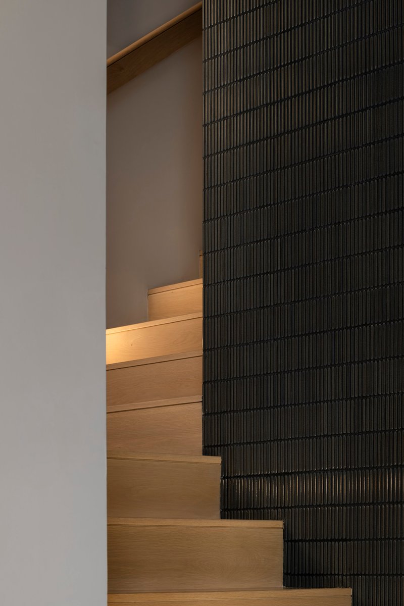 Timber staircase with integrated lighting alongside a black ribbed tile wall