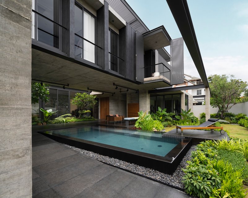 Garden courtyard showing the elevated dark volume cantilevering over the pool and terrace below