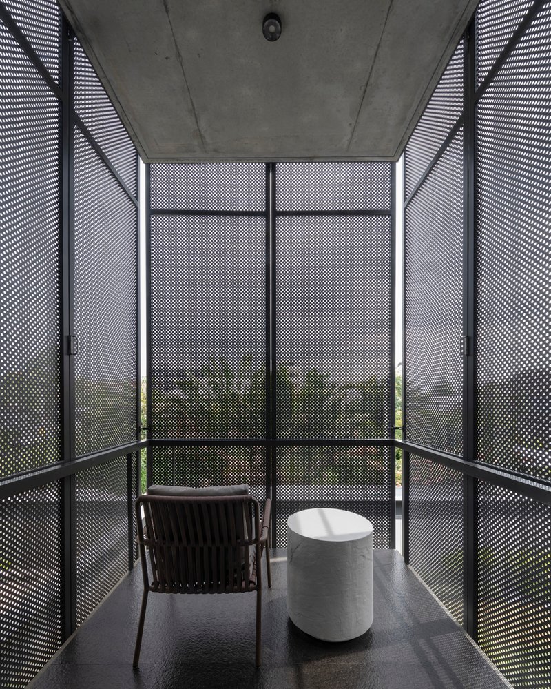 Enclosed balcony with perforated metal screens and exposed concrete ceiling at dusk