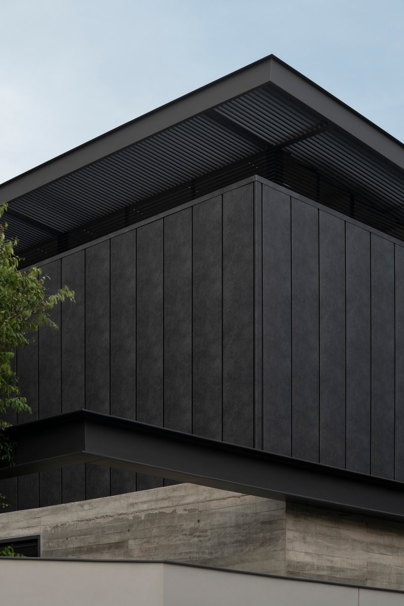 Corner detail of dark timber cladding with corrugated metal soffit and board-formed concrete wall below