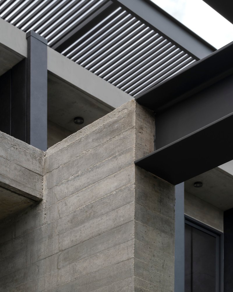Board-formed concrete corner column meeting dark metal beams and overhead louver screen