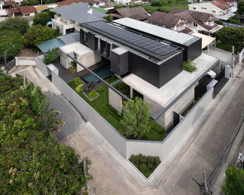 Aerial view of dark timber volume with solar panels surrounded by concrete terraces and landscaped courtyards