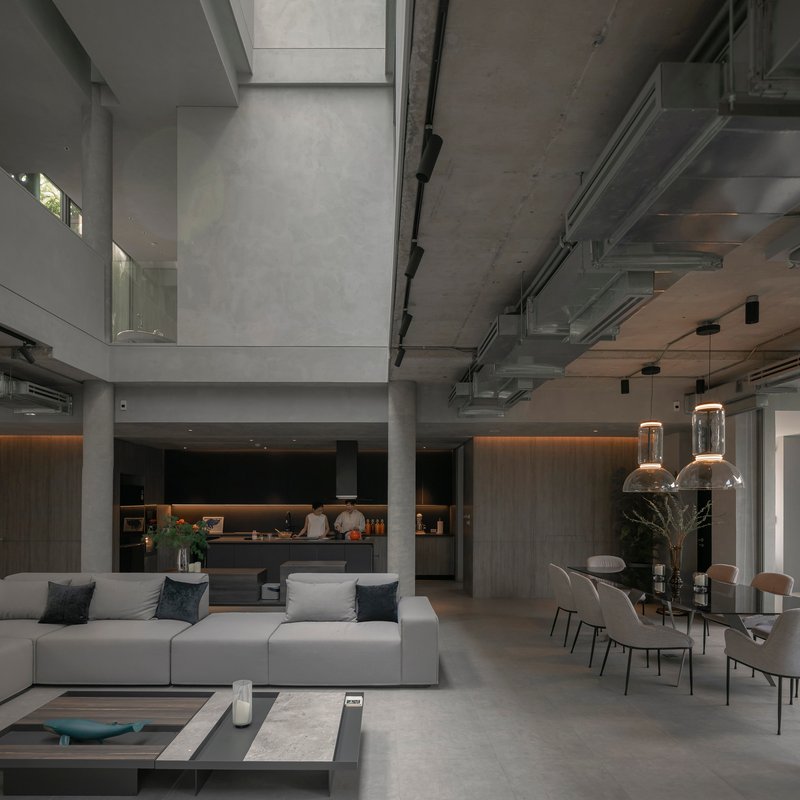 Open-plan living area with exposed concrete ceiling, pendant lights, and a kitchen beyond
