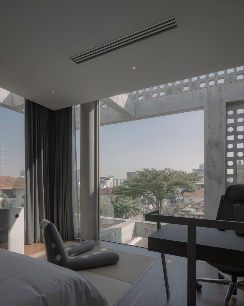 Bedroom window framed by perforated concrete beams overlooking neighborhood rooftops and a tree