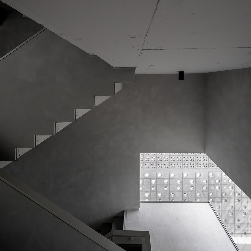 Looking up at cantilevered concrete stairs against a perforated glass block wall filtering natural light