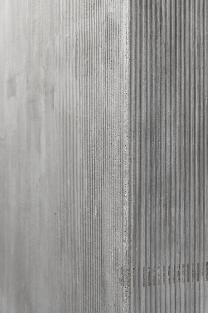 Close-up of cast concrete wall surface showing vertical ribbed formwork texture and seam joint