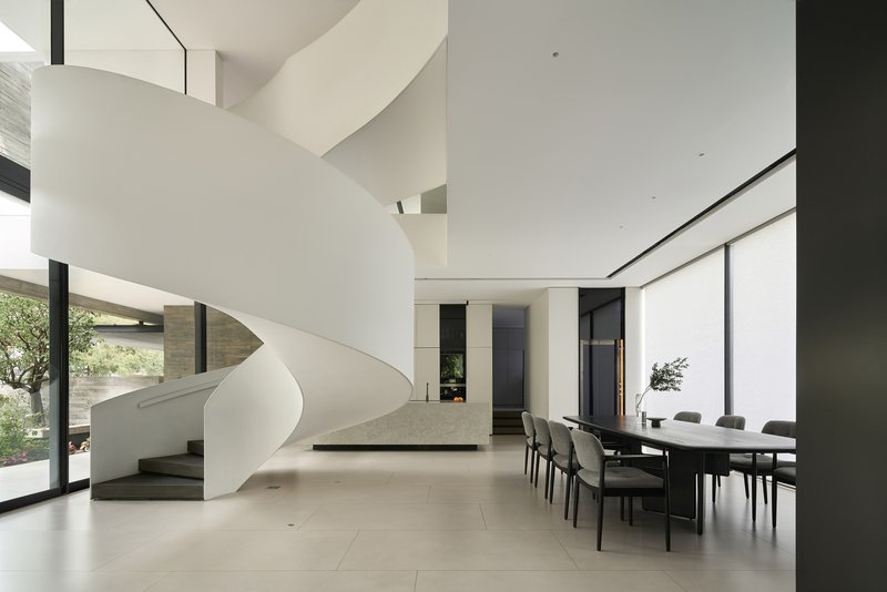 Open dining area beneath the sculptural white staircase with large windows framing the courtyard
