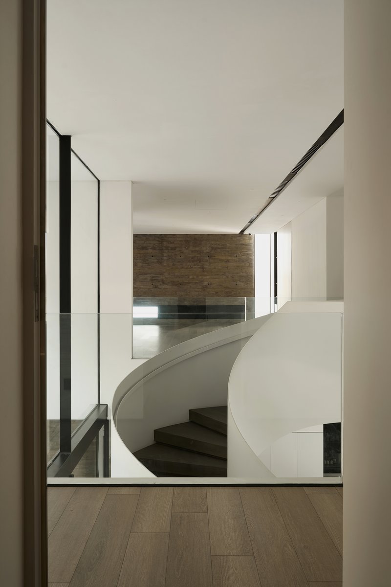 View through a doorway to the curved white staircase descending toward a timber-clad wall