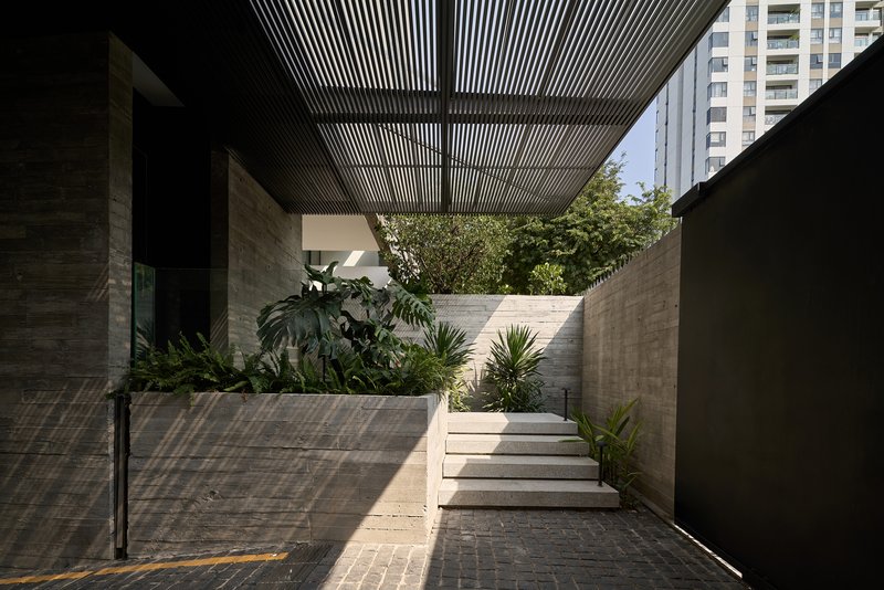 Exterior courtyard with timber slatted pergola casting shadows over planted beds and concrete steps